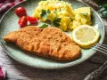 Perfekt gebratenes Putenschnitzel mit Kartoffelsalat, Tomaten und Zitrone auf einem Teller.