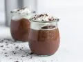 Zwei Gläser mit cremigem Schokopudding, gekrönt mit Schlagsahne und Schokostreuseln. Perfekt, um Schokopudding selber machen zu lernen!