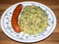 Omas Stielmus Rezept: deftiger Grünkohl mit Kartoffeln und einer herzhaften Bratwurst auf einem blau-weißen Teller.
