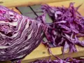 Ein halber Rotkohl liegt auf einem Holzbrett, daneben fein geschnittener Rotkohl für einen Salat.