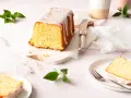 Saftiger zitronenkuchen kastenform mit Zuckerguss und bunten Streuseln, auf einem Marmorsockel, daneben ein Messer und ein Teller mit einem Stück Kuchen.