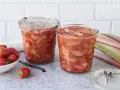 Zwei Gläser mit leckerem Rhabarberkompott, daneben frische Erdbeeren und Rhabarberstangen.