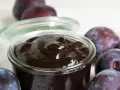 Ein Glas mit dunklem Pflaumenmus, umgeben von frischen Pflaumen. Perfekt für ein einfaches Pflaumenmus Rezept.