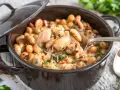 Eine Löffelportion von Omas dicken Bohnen mit Speck, cremig und herzhaft, dampft aus einem braunen Topf.