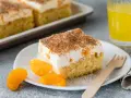 Ein saftiges Stück Fantakuchen-Rezept mit Mandarinen und Sahne, bestreut mit Zimt. Dazu ein Glas Fanta und frische Mandarinenstücke.