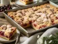 Ein saftiger Kirschstreuselkuchen im Blech, bestäubt mit Puderzucker. Daneben eine Schale frische Kirschen und ein Stück Kuchen auf einem Teller.