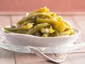 Omas Bohnensalat Rezept: Grüne Bohnen mit Zwiebeln in einer Schüssel auf einem Glasuntersetzer, daneben eine Gabel.