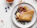 Buchweizen-Crêpes mit Schokoladensoße, Blaubeeren und Banane. Ein köstliches Beispiel für Buchweizen Rezepte, garniert mit Kokosraspeln und Pistazien.