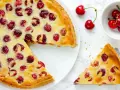 Ein köstlicher Pudding Kirsch Kuchen, mit frischen Kirschen belegt und goldbraun gebacken. Ein Stück wird gerade serviert.