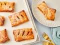 Goldbraune Apfeltaschen, bestäubt mit Puderzucker, warten auf dem Backblech und auf einem Teller. Ein köstliches Apfeltaschen Rezept zum Nachbacken.