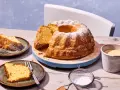 Ein goldbrauner Kartoffelkuchen mit Puderzucker bestreut, daneben zwei Teller mit Kuchenstücken, eine Tasse Kaffee und eine Kanne. Ein tolles Kartoffelkuchen Rezept!