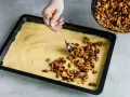 Eine Hand verteilt karamellisierte Walnüsse auf einem hellgelben Teig in einer Backform. Bald gibt es einen "friss dich dumm Kuchen"!