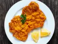 Ein knuspriges Schnitzel im Backofen, goldbraun paniert, mit Petersilie und Zitronenspalten auf einem weißen Teller serviert.