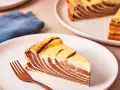 Ein Stück Zebrakuchen mit Quark, das auf einem Teller liegt, daneben eine Gabel.