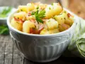 Ein einfacher Kartoffelsalat mit Speck und Petersilie in einer Schüssel, serviert auf einem Holztisch.