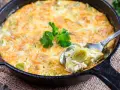 Ein goldbraunes Kartoffel-Lauch-Gratin in einer Gusseisenpfanne, mit einem Löffel herausgenommen, garniert mit Petersilie.