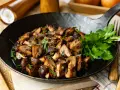 Gebratene Champignons in einer Pfanne, garniert mit frischer Petersilie. Ein köstliches Gericht, das zum Genießen einlädt.