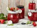 Gläser mit Erdbeer-Rhabarber-Marmelade, garniert mit frischen Erdbeeren und Blüten.
