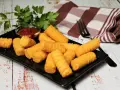 Goldbraune Kroketten, frisch zubereitet, liegen auf einem schwarzen Teller. Dazu gibt es Ketchup und frische Petersilie. Perfekt, um Kroketten selber machen zu lernen!