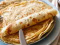 Ein Stapel goldbrauner Pfannkuchen, einer davon aufgerollt, mit Messer und Gabel. Perfekt für ein leckeres Pfannkuchen Rezept!