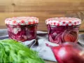Zwei Gläser mit eingelegten Zwiebeln, rot und weiß, stehen auf einem grauen Tuch. Frischer Dill und eine rote Zwiebel liegen davor.