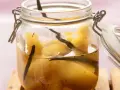 Ein Glas mit Quittenkompott, verfeinert mit Vanilleschoten. Die Fruchtstücke schimmern golden im Sirup.