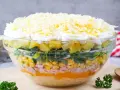 Schichtsalat rezept: Ein bunter Schichtsalat in einer Glasschüssel mit Ananas, Lauch, Mais, Schinken, Orange, Ei und Käse.