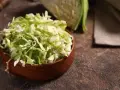 Fein geschnittener Spitzkohl in einer Holzschale, bereit, in der Pfanne gebraten zu werden. Ein halber Spitzkohl liegt im Hintergrund.