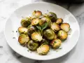 Knuspriger rosenkohl im airfryer, leicht gebräunt und mit Petersilie bestreut, auf einem weißen Teller serviert.