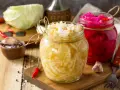 Zwei Gläser mit selbstgemachtem Sauerkraut und Rotkohl, daneben frischer Kohl, Knoblauch und Chilis.