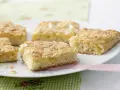 Saftiger mandelkuchen vom blech, goldbraun gebacken und mit knusprigen Mandelblättchen bestreut, liegt auf einer weißen Platte.