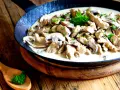 Putengeschnetzeltes mit Pilzen in cremiger Soße, garniert mit Petersilie, serviert in einer Pfanne auf rustikalem Holztisch.