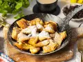 Ein fluffiger Kaiserschmarrn im Pfännchen, bestäubt mit Puderzucker. Perfekt für ein süßes Frühstück oder Dessert.