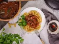 Herzhaftes Gulasch gemischt Rezept mit Fusilli, garniert mit Petersilie. Daneben ein kleiner Teller mit Preiselbeeren.