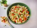 Ein bunter Nudelsalat mit Fleischwurst, Erbsen, Mais und Paprika in einer grünen Schüssel.