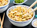 Ein Schüsselchen mit friss dich dumm Salat, Nudeln, Gemüse und Erdnüssen, bereit zum Genießen mit Stäbchen.