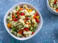 Frischer blumenkohl salat mit Paprika, Karotten und Kräutern, serviert in einer weißen Schüssel. Daneben eine kleine Schale mit Dip.