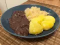 Ein Teller mit deftigem Essen: dunkle Soße, Sauerkraut und Salzkartoffeln. Erinnert an die gute, alte tote Oma.