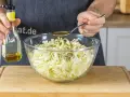 Ein Löffel Öl wird über den fein geschnittenen Spitzkohl gegeben, der für Omas Spitzkohlsalat vorbereitet wird.