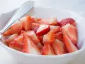 Schüssel mit marinierten Erdbeeren, die mit einem Löffel serviert werden. Saftige, rote Erdbeerstücke glänzen im Licht.
