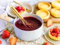 Frisch zubereiteter Tortenguss in einem Topf, bereit, um Obstkuchen zu verfeinern. Daneben liegen frische Erdbeeren und leere Tartelettes.