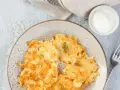 Knusprige Kartoffelpuffer, im Waffeleisen goldbraun gebacken, liegen auf einem Teller. Dazu ein Schälchen mit Sour Cream und ein Gabel.