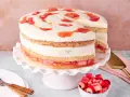 Eine köstliche Erdbeer Rhabarber Torte mit Sahne und Fruchtstücken, auf einem rosa Tortenständer präsentiert.