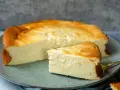 Ein saftiger Quarkkuchen ohne Boden, goldbraun gebacken, liegt auf einem Teller. Ein Stück ist bereits angeschnitten.