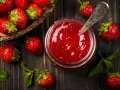 Frische Erdbeeren und ein Glas selbstgemachte Erdbeermarmelade, bereit zum Einkochen. Ein Löffel steckt in der Marmelade.