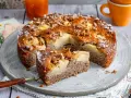 Ein saftiger Apfel-Birnen-Kuchen, bestreut mit Nüssen und Puderzucker, wird auf einem Teller serviert. Ein Stück ist bereits herausgeschnitten.