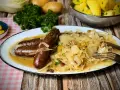 Deftige Bratwürste mit Zwiebeln auf bayrisch Kraut, garniert mit Petersilie. Dazu Salzkartoffeln und Senf.