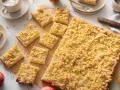 Ein frisch gebackener Apfelkuchen mit Streusel, aufgeteilt in rechteckige Stücke, daneben Äpfel und eine Tasse Kaffee.