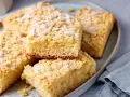 Saftiger Streuselkuchen vom Blech, mit Puderzucker bestäubt, liegt auf einem Teller.