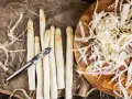 Frischer weißer Spargel wird geschält, die Spargelschalen liegen daneben. Ein Sparschäler liegt auf den Spargelstangen.